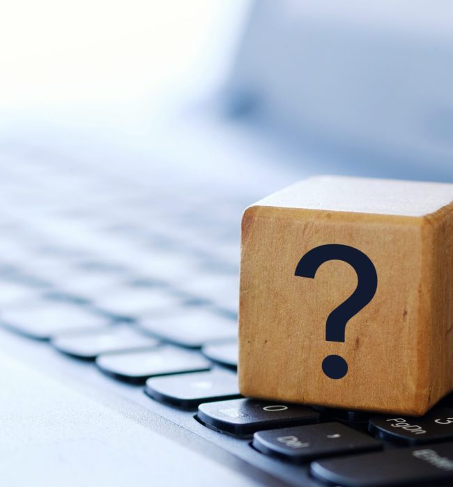 A question mark on a wooden cube on a computer keyboard, with a blurred background and shallow depth of field.